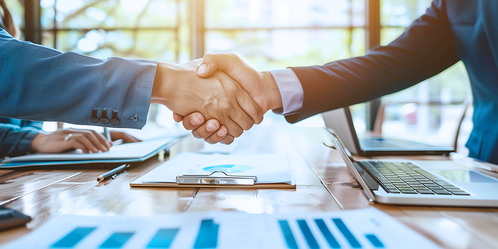 Les professionnels des entreprises serrant la main dans une table de réunion, entouré d\'ordinateurs portables et de documents, symbolisant des partenariats réussis dans l\'industrie des outils électriques.